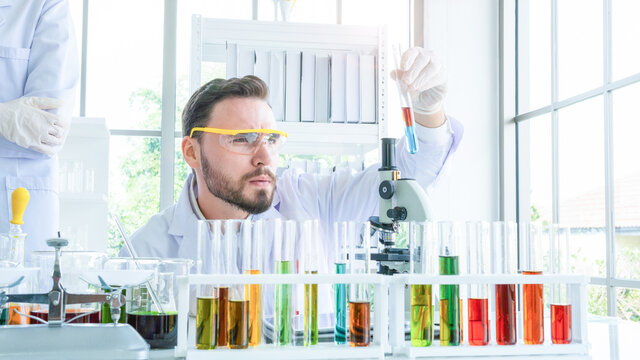 male scientist holding a tube with liquid substance. Man Research is working in the Laboratory with foreground of tube and Beaker of liquid substance.
