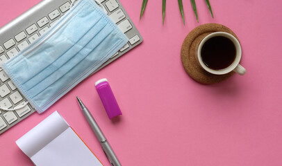 Top view of pink office desk with keyboard, medical face mask, coffee and stationery.