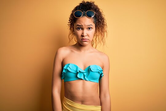 Young beautiful american woman on vacation wearing bikini over isolated yellow background skeptic and nervous, frowning upset because of problem. Negative person.