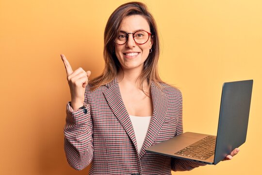 Young beautiful woman holding laptop smiling happy pointing with hand and finger to the side