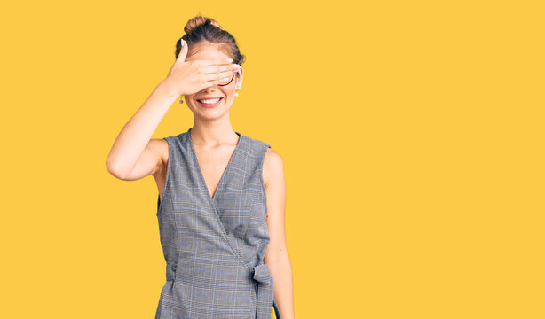 Beautiful caucasian woman with blonde hair wearing business clothes and glasses smiling and laughing with hand on face covering eyes for surprise. blind concept.