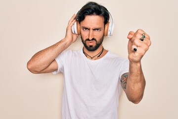 Fototapeta premium Young handsome hispanic man wearing headphones listening to music over isolated background annoyed and frustrated shouting with anger, crazy and yelling with raised hand, anger concept
