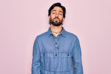 Young handsome hispanic bohemian man wearing hippie style over pink background Relaxed with serious expression on face. Simple and natural looking at the camera.