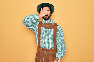 Young handsome man wearing tratidional german octoberfest custome for Germany festival covering...