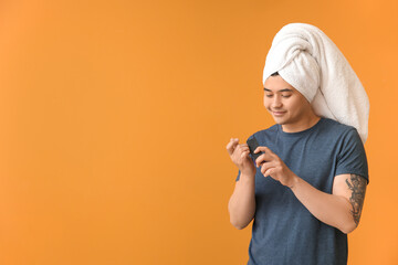 Funny Asian man doing manicure on color background