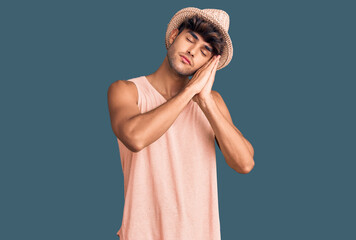 Young hispanic man wearing summer hat sleeping tired dreaming and posing with hands together while smiling with closed eyes.