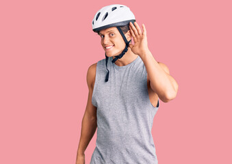 Young handsome man wearing bike helmet smiling with hand over ear listening an hearing to rumor or gossip. deafness concept.