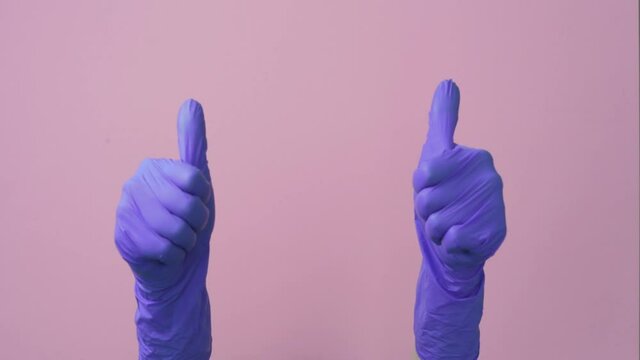 Two arms. Thumb up in surgical, medical gloves, gesture. Pink background.