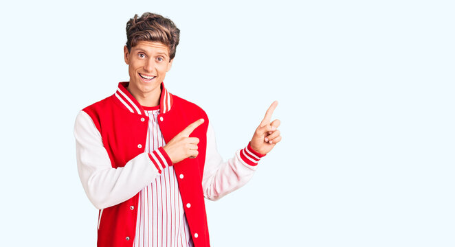 Young handsome man wearing baseball uniform smiling and looking at the camera pointing with two hands and fingers to the side.