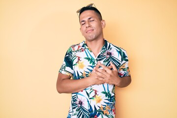 Young handsome latin man wearing summer clothes smiling with hands on chest with closed eyes and grateful gesture on face. health concept.