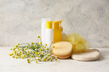 Cosmetics with chamomile flowers and bathing supplies on light background
