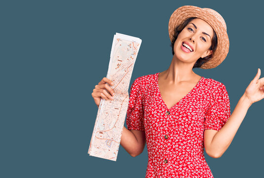 Young beautiful woman wearing summer hat holding map smiling happy pointing with hand and finger to the side