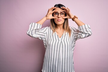 Young beautiful woman wearing casual striped t-shirt and glasses over pink background Trying to open eyes with fingers, sleepy and tired for morning fatigue
