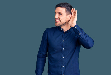 Obraz premium Young handsome man wearing casual shirt smiling with hand over ear listening an hearing to rumor or gossip. deafness concept.