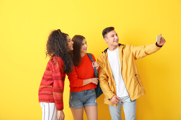 Young students taking selfie on color background