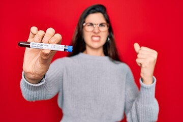 Young beautiful girl wearing glasses holding laboratory blood sample of coronavirus disease annoyed and frustrated shouting with anger, crazy and yelling with raised hand, anger concept