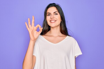 Young beautiful brunette woman wearing casual white t-shirt over purple background smiling positive doing ok sign with hand and fingers. Successful expression.