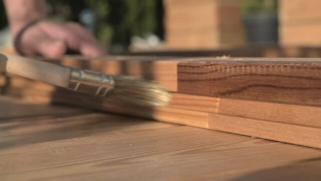 Close Up Of Painter Brushing Protective Layer Of Transparent Lacquer On Newly Built Wooden Outdoor Project.