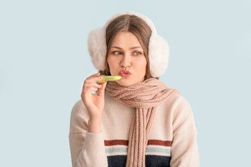 Beautiful young woman with lip balm on light background