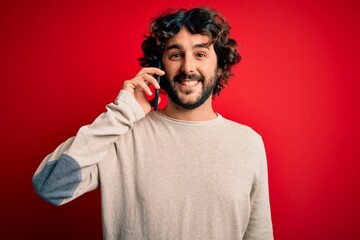 Handsome man with beard having conversation talking on the smartphone over red background with a happy face standing and smiling with a confident smile showing teeth