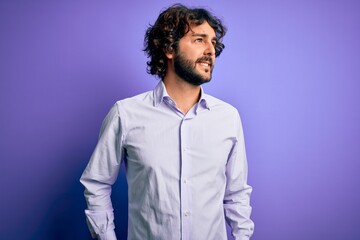 Young handsome business man with beard wearing shirt standing over purple background looking away to side with smile on face, natural expression. Laughing confident.