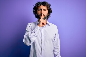 Young handsome business man with beard wearing shirt standing over purple background asking to be quiet with finger on lips. Silence and secret concept.