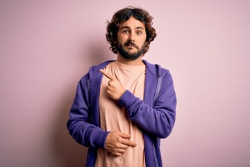 Young handsome sporty man with beard wearing casual sweatshirt over pink background Pointing aside...