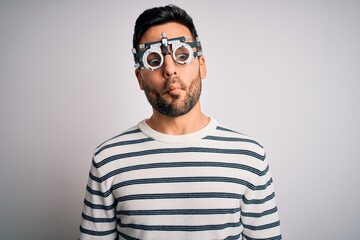 Young handsome man with beard wearing optometry glasses over isolated white background making fish face with lips, crazy and comical gesture. Funny expression.