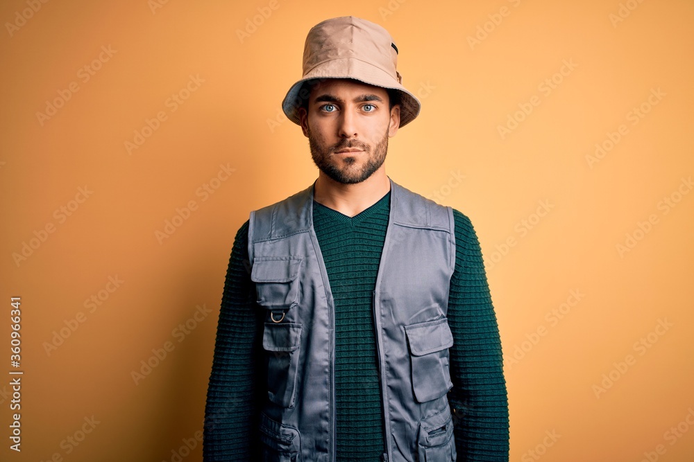 Canvas Prints Handsome tourist man with beard on vacation wearing explorer hat over yellow background Relaxed with serious expression on face. Simple and natural looking at the camera.