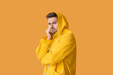 Displeased young man in raincoat on color background