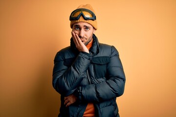 Young handsome skier man with beard wearing snow sportswear and ski goggles thinking looking tired and bored with depression problems with crossed arms.