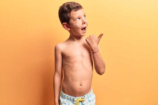 Cute blond kid wearing swimwear pointing thumb up to the side smiling happy with open mouth