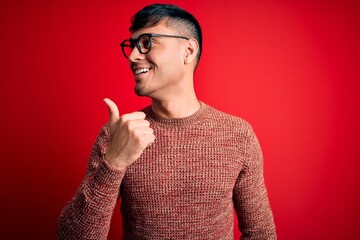 Young handsome hispanic man wearing nerd glasses over red background smiling with happy face...