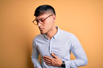 Young handsome hispanic business man wearing nerd glasses over yellow background with hand on...