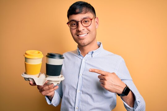 Young scholarship holder business man holding take away coffee over isolated yellow background very happy pointing with hand and finger