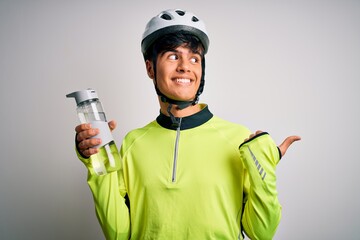 Young handsome cyclist man wearing security bike helmet drinking bottle of water pointing and showing with thumb up to the side with happy face smiling