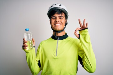 Young handsome cyclist man wearing security bike helmet drinking bottle of water doing ok sign with fingers, excellent symbol