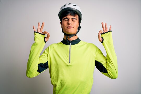 Young handsome cyclist man wearing security bike helmet over isolated white background relax and smiling with eyes closed doing meditation gesture with fingers. Yoga concept.