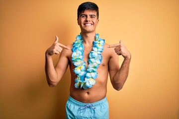 Young handsome tourist man on vacation wearing swimwear and hawaiian lei flowers looking confident...