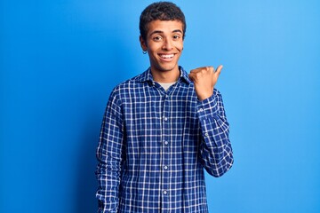 Young african amercian man wearing casual clothes smiling with happy face looking and pointing to the side with thumb up.