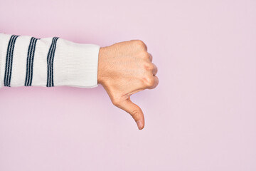 Hand of caucasian young man showing fingers over isolated pink background doing thumbs down rejection gesture, disapproval dislike and negative sign