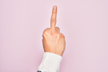 Hand of caucasian young man showing fingers over isolated pink background showing provocative and rude gesture doing fuck you symbol with middle finger