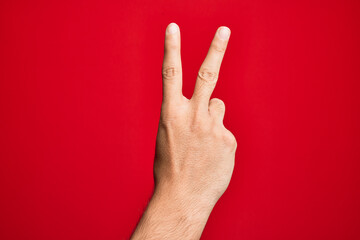 Hand of caucasian young man showing fingers over isolated red background counting number 2 showing two fingers, gesturing victory and winner symbol