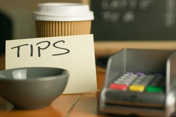 Closeup shot of a bowl near a contactless pdq machine and a tips note leaning on a coffee cup