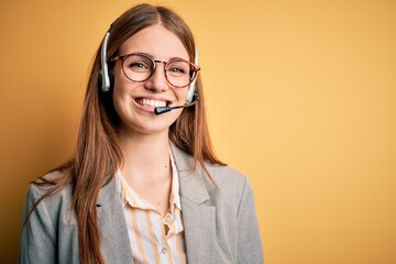 Young redhead call center agent woman overworked wearing glasses using headset with a happy and...