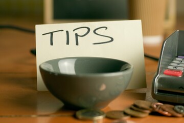 Closeup shot of a bowl near a contactless pdq machine and a tips note leaning on a coffee cup