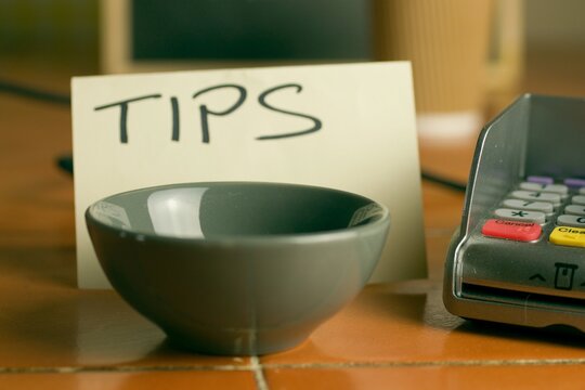 Closeup shot of a bowl near a contactless pdq machine and a tips note leaning on a coffee cup