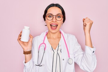 Young beautiful doctor woman with blue eyes wearing stethoscope holding medicine pills screaming proud and celebrating victory and success very excited, cheering emotion