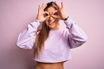 Young beautiful sport woman wearing sweatshirt over pink isolated background doing ok gesture like binoculars sticking tongue out, eyes looking through fingers. Crazy expression.