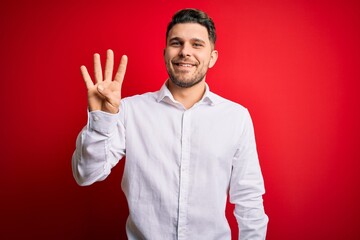 Young business man with blue eyes wearing elegant shirt standing over red isolated background showing and pointing up with fingers number four while smiling confident and happy.